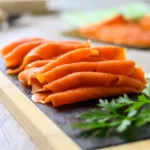 West Coast Seafood Sample: Image of thinly sliced cold smoked salmon lox arranged artistically on a dark slate charcuterie board. The salmon's rich, pinkish-orange color contrasts beautifully against the slate, enhancing its visual appeal. Sprigs of fresh, vibrant green parsley add a pop of color and texture, suggesting freshness and enhancing the overall aesthetic of the culinary presentation