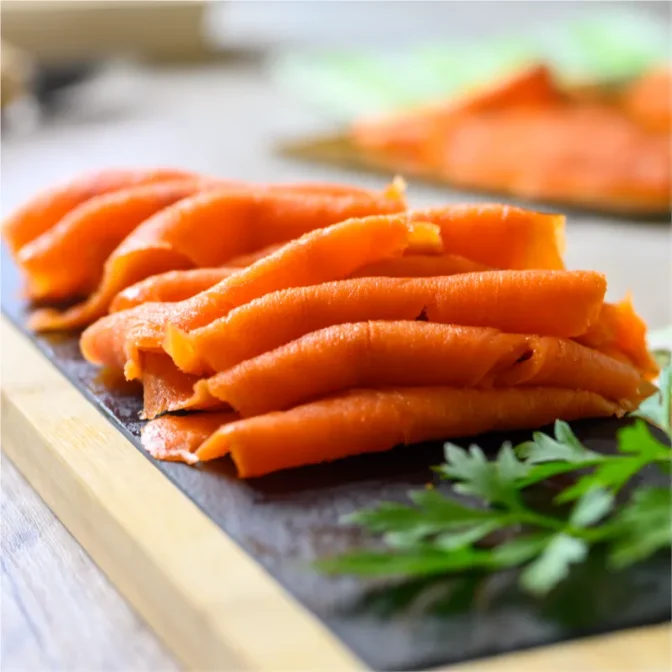 West Coast Seafood Sample: Image of thinly sliced cold smoked salmon lox arranged artistically on a dark slate charcuterie board. The salmon's rich, pinkish-orange color contrasts beautifully against the slate, enhancing its visual appeal. Sprigs of fresh, vibrant green parsley add a pop of color and texture, suggesting freshness and enhancing the overall aesthetic of the culinary presentation