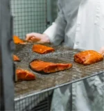 St Jean's worker pulling racks of smoked salmon from the smokehouse racks